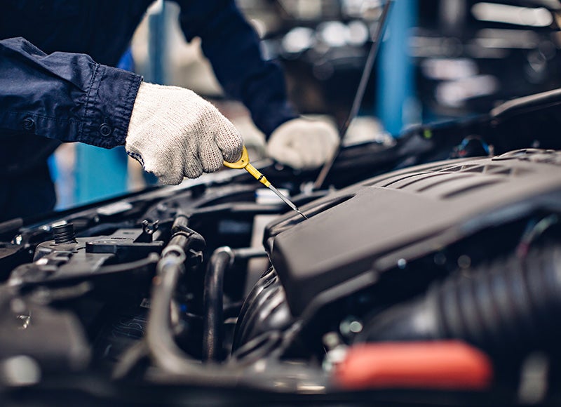 Gloved hand pulling a yellow dipstick from a car engine to check oil.